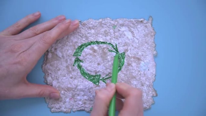女人的手用绿色的毡尖笔画出了重复使用的标志。在再生纸上画画。可重复使用的纸张，背景，纹理。关爱环境、