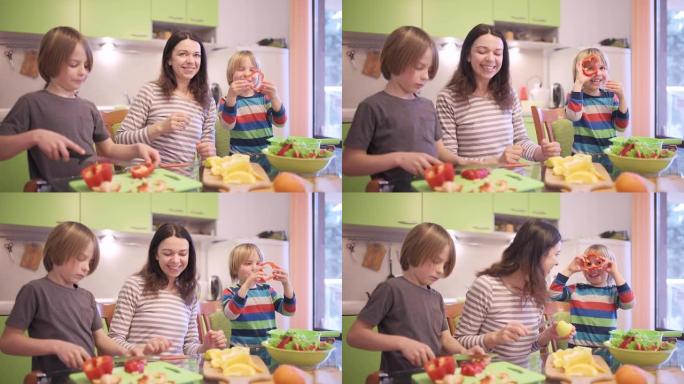 幸福的年轻家庭，美丽的母亲和两个孩子，可爱的学龄前男孩和在校男孩在阳光明媚的厨房里一起做饭。