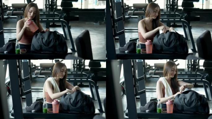特写镜头，一名年轻女子从包里准备东西，早上戴着无线蓝牙耳塞立体声音乐在健身俱乐部接受训练