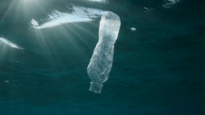 塑料污染，被丢弃的塑料瓶在黎明时分在阳光的照射下慢慢漂浮在水面下。蓝色水中的塑料瓶。海洋中的塑料垃圾