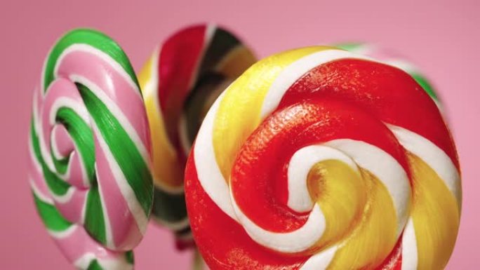 粉红色背景上旋转的圆形焦糖棒棒糖。各色水果味糖果。孩子们的生日甜点。慢动作准备，4K 59.94帧/