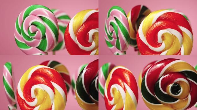 粉红色背景上旋转的圆形焦糖棒棒糖。各色水果味糖果。孩子们的生日甜点。慢动作准备，4K 59.94帧/