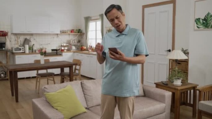 记忆力不好的亚洲老年男性的慢动作在客厅的沙发上寻找手机。他取下枕头，发现手机在后面