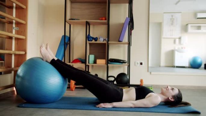 一个女人在健身爽肤球上做肌肉锻炼。在理疗工作室
