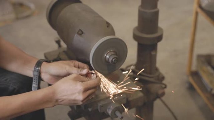 这位亚洲工人正在为没有安全手套的小型铜器进行磨削。工厂火花研磨机。手技。