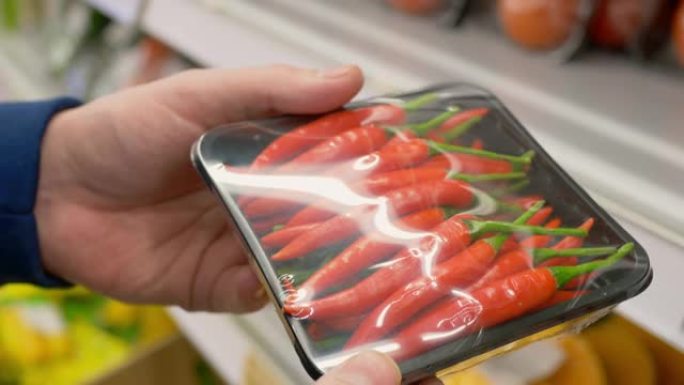 从商店柜台的架子上拍摄了塑料包装中的红辣椒的特写镜头，一名男子在市场上选择蔬菜在家做饭