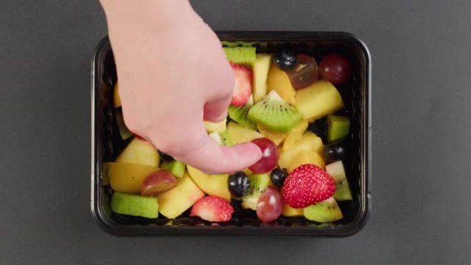 烹饪水果沙拉特写。带走餐点俯视图，在封闭的一次性容器中运送食物，营养均衡。午餐盒中的新鲜部分，素食。