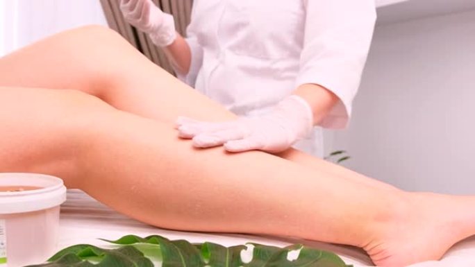 在美容师的手套，身体护理概念中，在水疗沙龙中去除头发后，关闭女性腿的视频。后epil乳液奶油油产品。