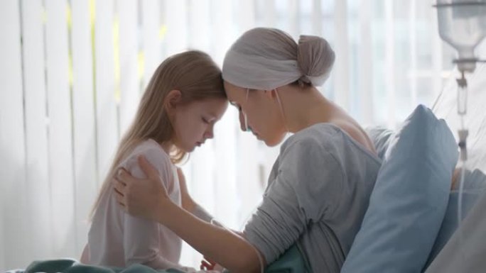 与小女儿坐在医院病床上的癌症年轻女子的侧视图