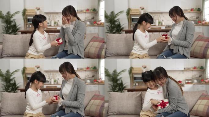 惊讶的亚洲母亲拥抱女儿在家中获得母亲节礼物的慢动作。当妈妈遮住眼睛时，女孩从背后展示礼物