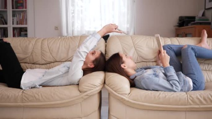 十几岁的女孩双胞胎姐妹在家观看社交媒体上的智能手机躺在沙发上正面交锋
