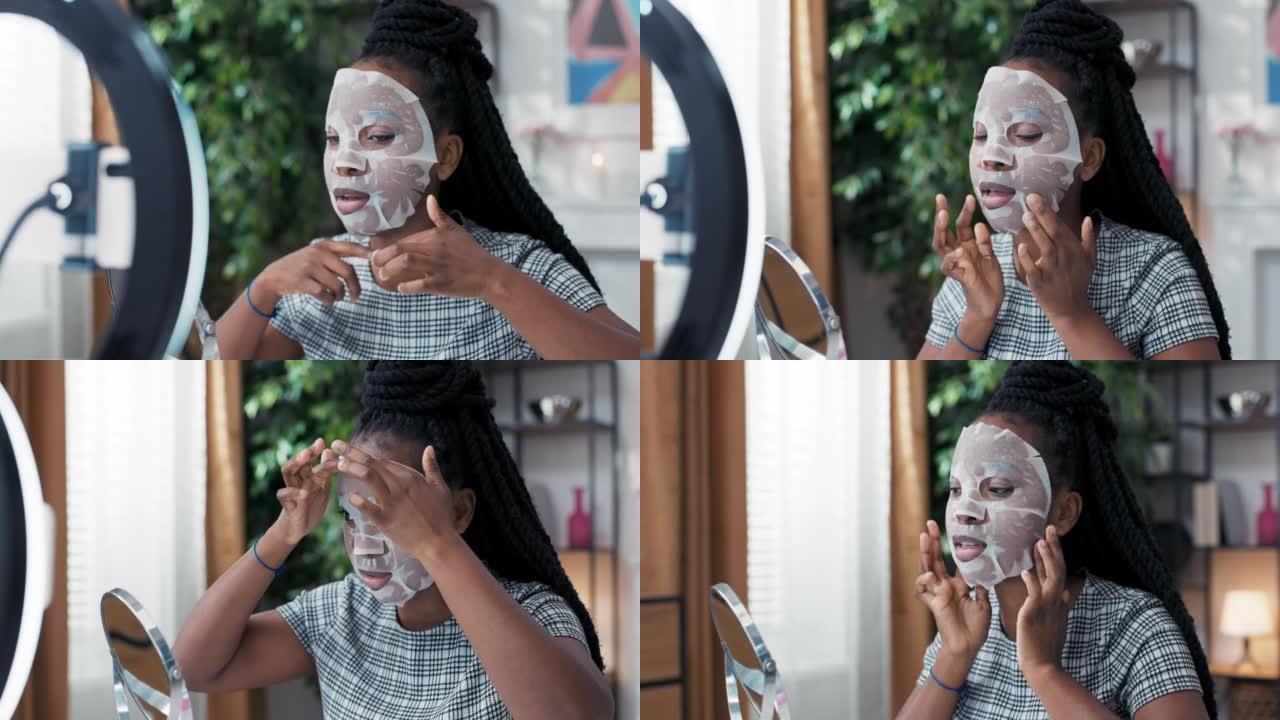一位美丽的年轻非裔美国妇女正在家里享受美容护理，在她的脸上涂上一层面膜。她为社交媒体频道录制了护肤教