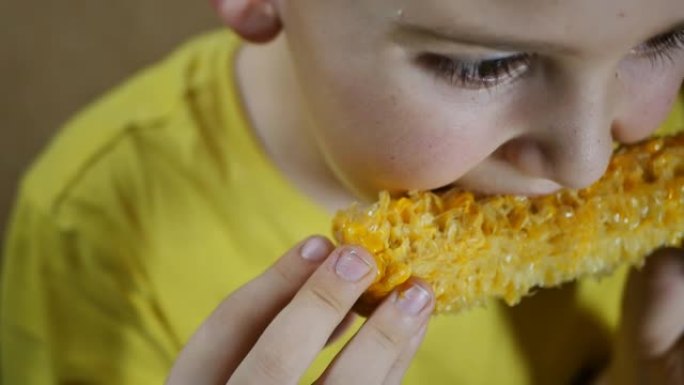 肖像一个十几岁的男孩吃煮熟的玉米，并饶有兴趣地看着屏幕