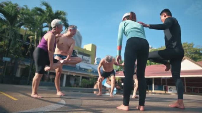 亚洲中国高级男子试图平衡自己的站立，单腿热身运动在游泳池边游泳课前向游泳教练学习
