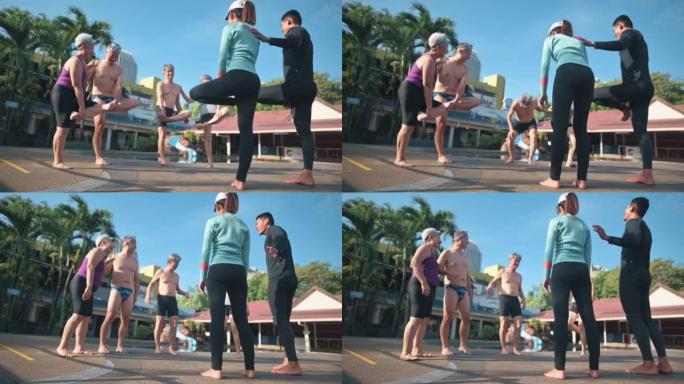 亚洲中国高级男子试图平衡自己的站立，单腿热身运动在游泳池边游泳课前向游泳教练学习