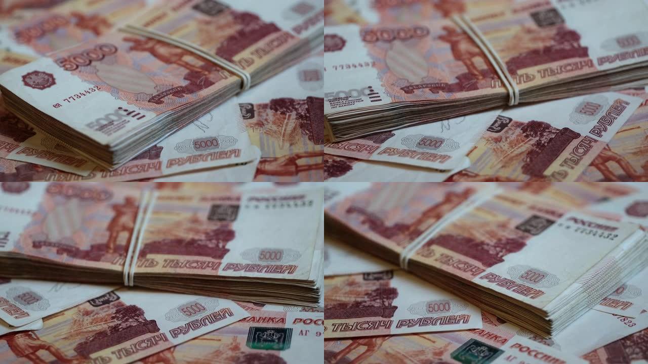 一捆用橡皮筋绑着的千分之五的俄罗斯卢布钱躺在一个旋转平台上，上面覆盖着5000卢布的钞票。