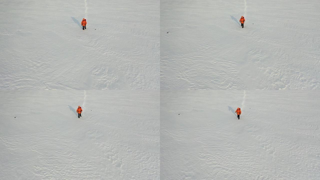 空中-一个背着背包和棍棒的人走过白雪皑皑的沙漠，留下了一连串的脚印。在极冷条件下生存的概念