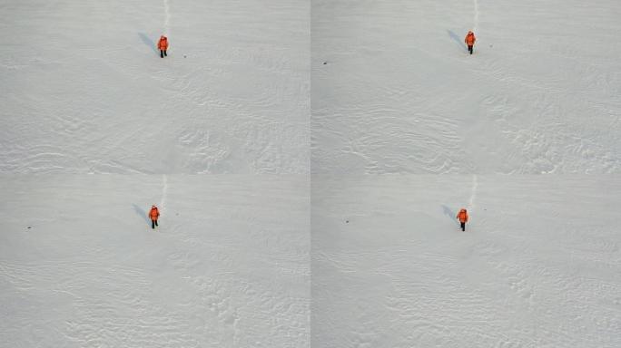 空中-一个背着背包和棍棒的人走过白雪皑皑的沙漠，留下了一连串的脚印。在极冷条件下生存的概念