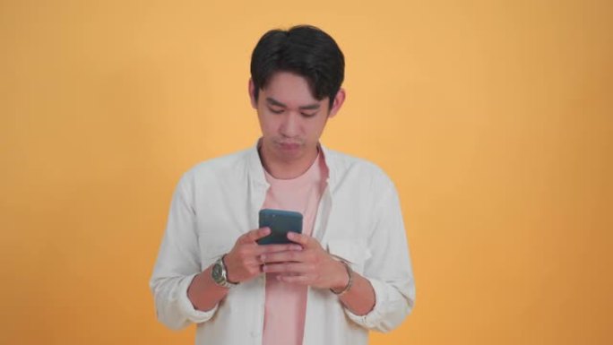 震惊，惊讶的亚洲年轻人使用移动智能手机在孤立的工作室黄色背景工作室肖像。面部表情，惊讶于激动人心的微