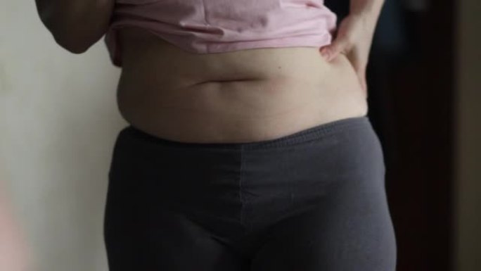 女性双手触摸肥胖的腹部，测量身体体积和体重