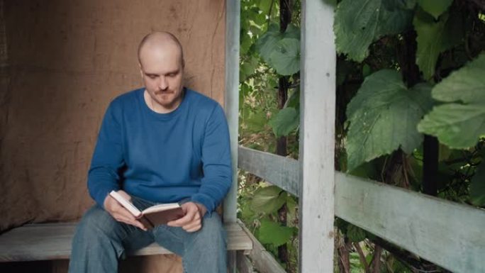 男人正在读一本坐在村舍门廊上的纸质书