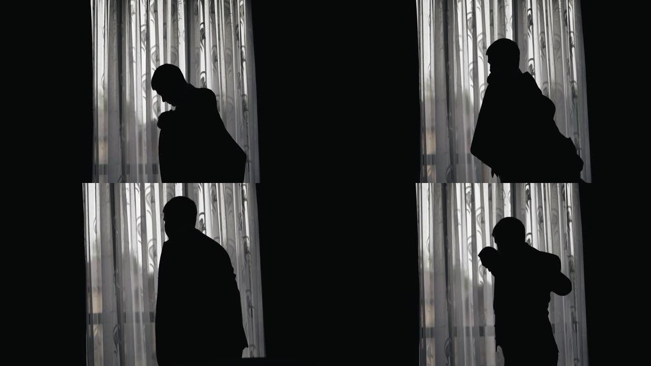 一个穿着夹克站在窗前的男人的轮廓。窗户发出的昏暗的光线