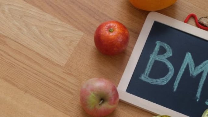 黑板上的缩写BMI (身体质量指数) 和一些水果，它周围有一个水瓶和卷尺。