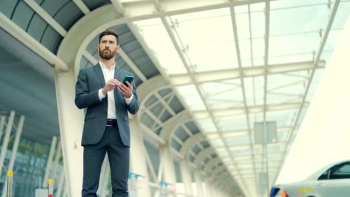 商人站在背景上的一个现代火车站机场的正式西装使用应用程序手机。