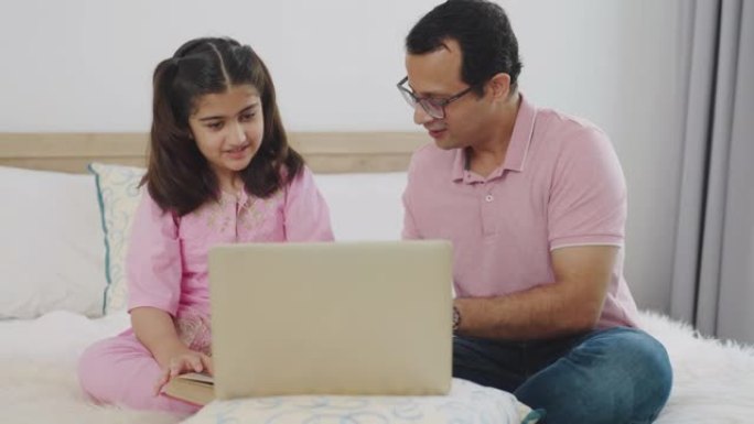 印度父亲在女儿的在线会议期间帮助女儿，并在卧室使用笔记本电脑。