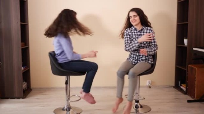 十几岁的女孩双胞胎姐妹在家里的椅子上互相拍手很开心
