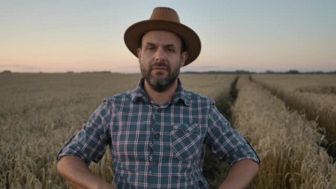 肖像农民留着帽子的男人站在麦田里。农场工人。日落的天空。肖像高加索农民男子穿着帽子的格子衬衫看着相机