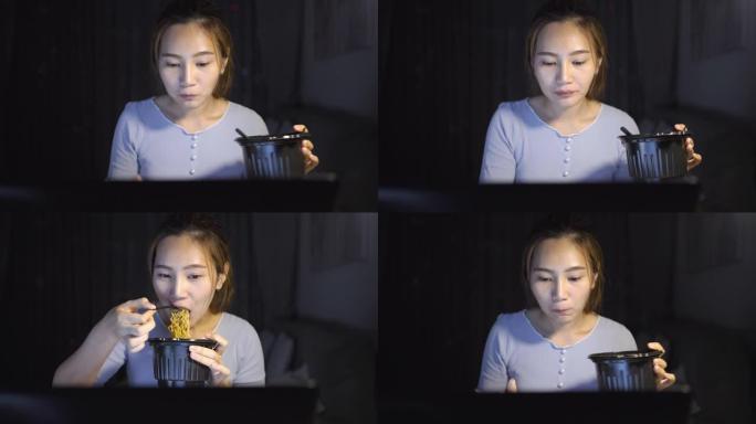 亚洲自由职业者聪明的女商人晚上在家客厅里在笔记本电脑上工作时吃方便面快乐的亚洲女孩坐在桌子上加班享受