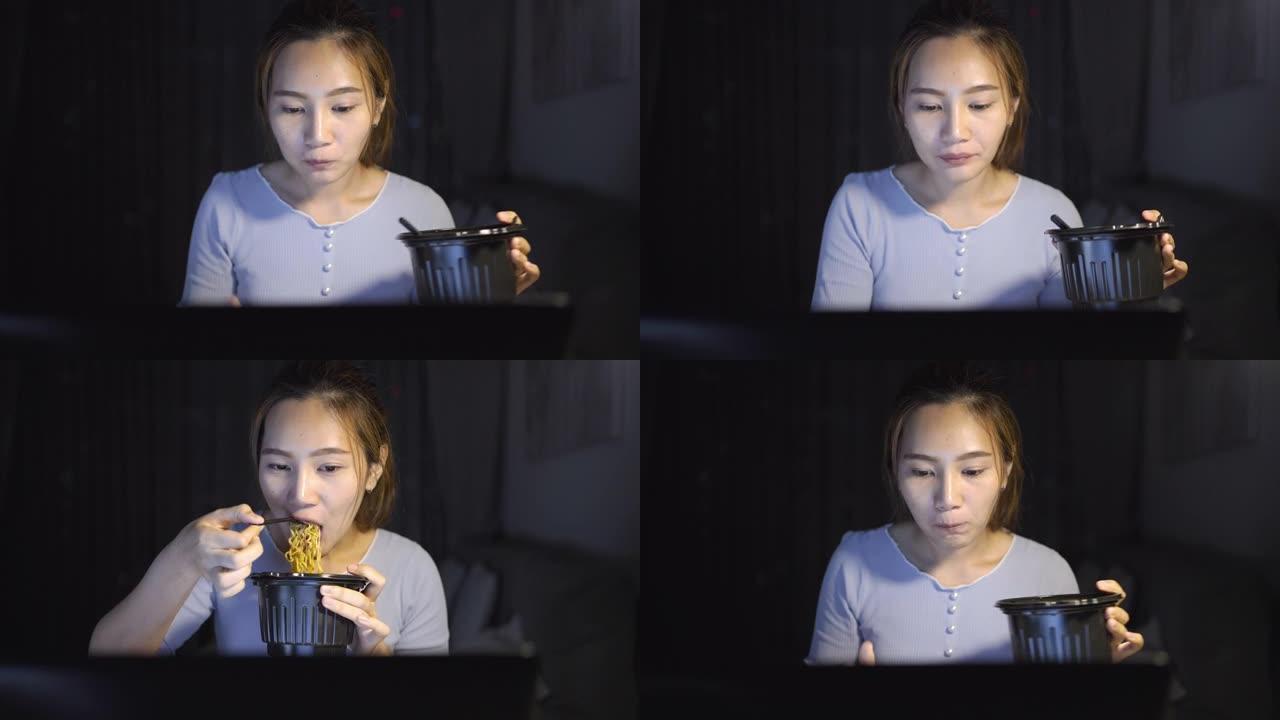 亚洲自由职业者聪明的女商人晚上在家客厅里在笔记本电脑上工作时吃方便面快乐的亚洲女孩坐在桌子上加班享受