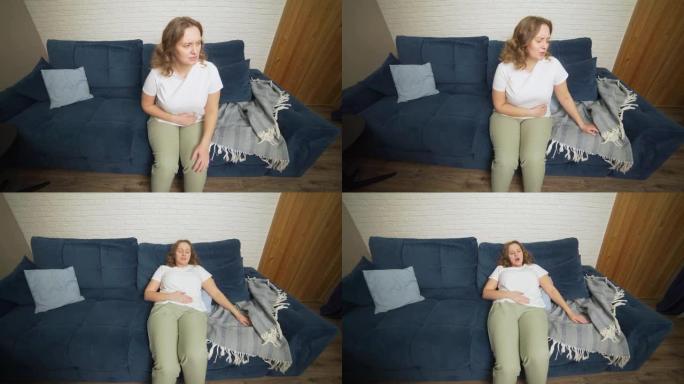 穿着白色t恤的女人坐在蓝色的沙发上，痛苦地抱着肚子。月经，怀孕，腹泻，暴食。脸因疼痛而抽筋