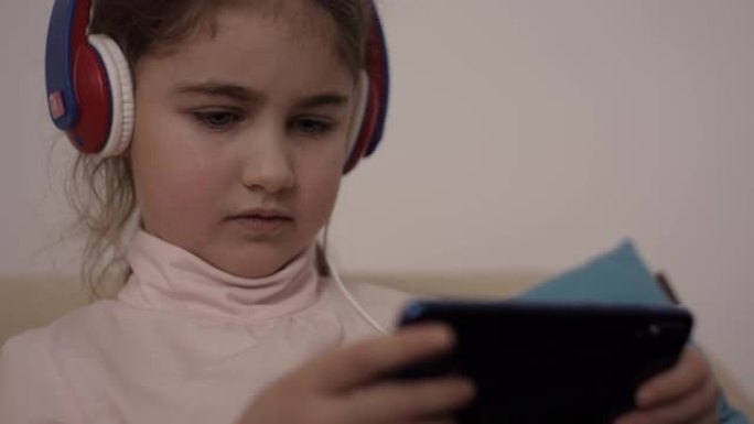 孩子开心地用手机玩游戏。戴着耳机的小女孩在手机上玩视频游戏。青少年在智能手机上玩视频游戏。危害精神儿