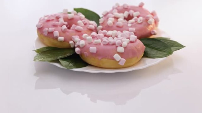 旋转镜头的白色美味美味甜甜甜圈，彩色洒在白色背景上。彩色磨砂粉色甜甜圈。什锦甜甜圈。粉红色的釉面和撒