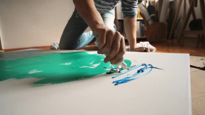 高加索男性艺术家从画布上的油漆管中挤压油漆