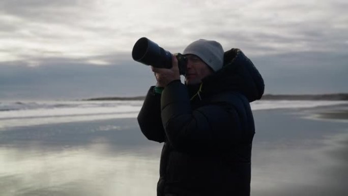 摄影师举起相机在潮湿的海滩上拍摄