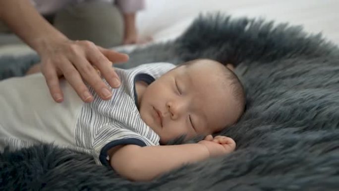 4K 50fps，近距离新生儿，2个月大，亚洲人睡在黑灰色的地毯上，母亲的手放在胸前，使婴儿睡得很好