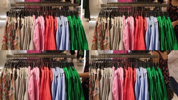 顾客在购物中心的服装店购物，各种各样的彩色衬衫挂在商店的栏杆上。每天买东西穿，女人爱经常换衣柜