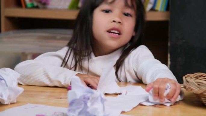 心烦意乱的小女孩在家里画了一幅五颜六色的画，把桌子上的纸弄皱了。在冠状病毒大流行期间厌倦在线学习和家