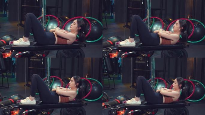 亚洲年轻女运动员在健身椅上做仰卧起坐。健身女士做腹肌仰卧起坐。在健身房做腹肌锻炼。