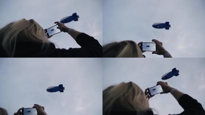 一个女人看着天空，用手机从空中盘旋的大型飞艇上起飞。