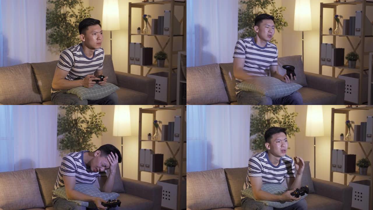 心烦意乱的亚洲男子拍打枕头，双手拿着操纵杆沮丧地抱着头，因为他失去了家里客厅沙发上的电子游戏