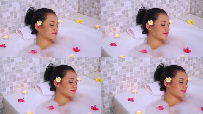 一个年轻美丽的亚洲女人在私人浴缸上放松的视频片段，用肥皂泡、素馨花和蜡烛