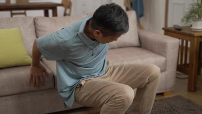 中国成熟男子移动坐在沙发上休息，同时下背部疼痛，呻吟着非常不适。老年人滑倒和跌倒风险的概念