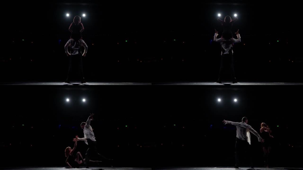 女舞者坐在男人的肩膀上，同步的手动作，翻转，旋转和转身，在伸展的手臂上跳舞。在黑暗的大厅前的舞台上跳
