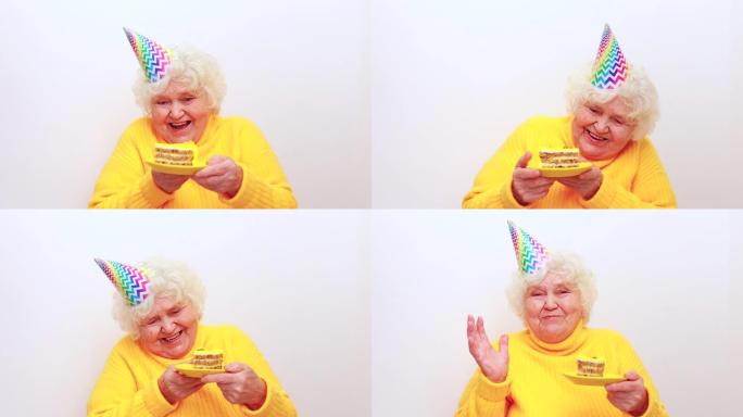 有礼物的老妇人穿着黄色毛衣和喇叭帽在白色背景上拿着盘子，蛋糕上有烟火