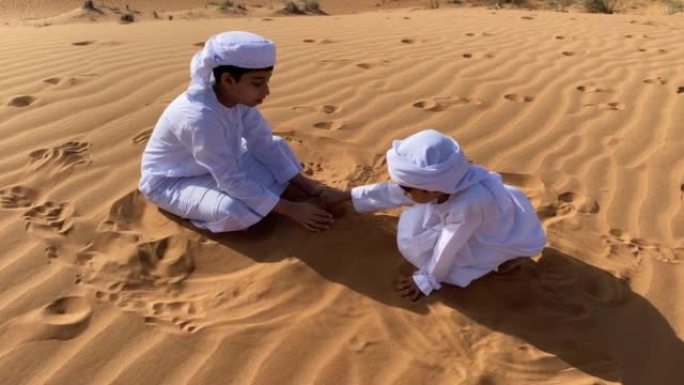 两个Emarati孩子在沙漠中玩沙子