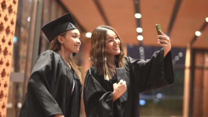 亚洲十几岁的女孩穿着毕业礼服布带着心情开心。穿黑色毕业礼服的人持有毕业证书。